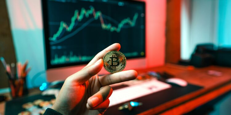 Cryptocurrency sportsbooks, fingers holding crypto coin in front of a monitor