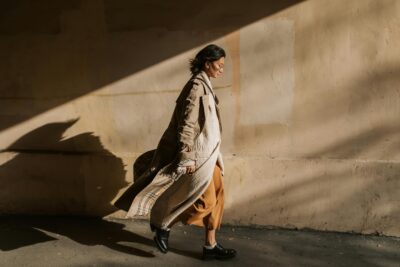 sustainable fashion, woman walking with shadow against a wall, burberry coat, linen coat, doc martens