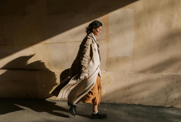 sustainable fashion, woman walking with shadow against a wall, burberry coat, linen coat, doc martens