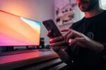 screen time rituals, hands holding mobile phone in front of curved monitor screen