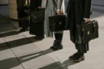 quiet luxury silhouttes, four people standing with briefcases and monochromatic outfits