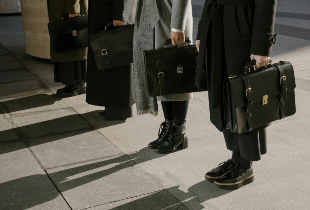 quiet luxury silhouttes, four people standing with briefcases and monochromatic outfits
