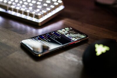 closeup photo of turned on smartphone near keyboard displaying twitch stream social apps chat stream