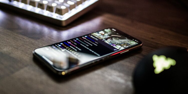 closeup photo of turned on smartphone near keyboard displaying twitch stream social apps chat stream