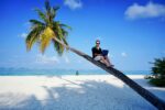 a man sitting on a palm tree using a laptop for workation
