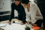 man and woman leaning on table staring at white board on top of table having a meeting for logo design