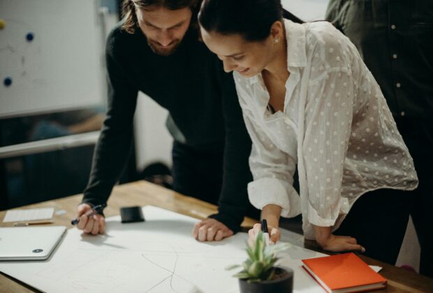 man and woman leaning on table staring at white board on top of table having a meeting for logo design