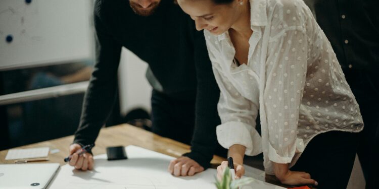 man and woman leaning on table staring at white board on top of table having a meeting for logo design