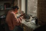 woman doing calligraphy with a cat in front of a window