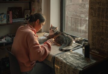 woman doing calligraphy with a cat in front of a window