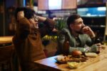 man holding his head at a bar while watching live sports tv