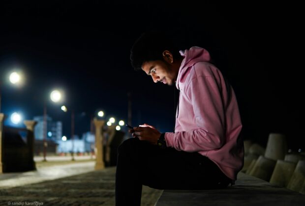 a man sitting on a bench looking at his cell phone for digital stress relief activities