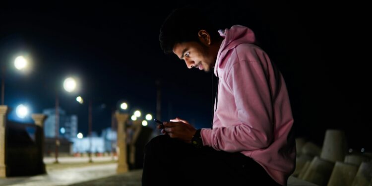 a man sitting on a bench looking at his cell phone for digital stress relief activities