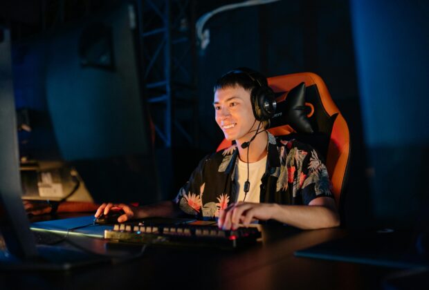 photo of a man playing on a computer and sitting on a gaming chair while smiling