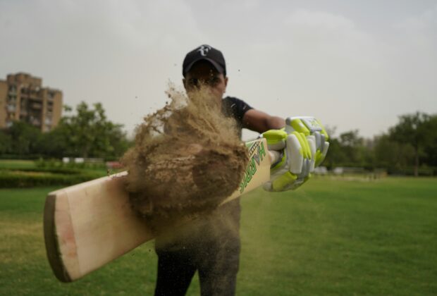 indian cricket player stricking a ball covered in mud