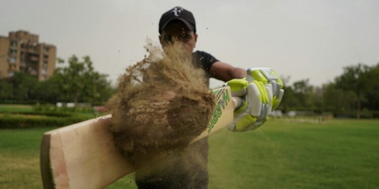indian cricket player stricking a ball covered in mud