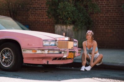 Woman in vintage clothes aesthetic sitting next to a pink cadillac