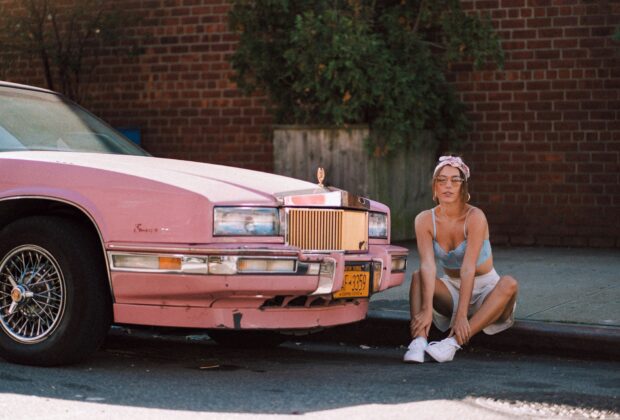 Woman in vintage clothes aesthetic sitting next to a pink cadillac