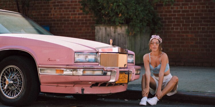 Woman in vintage clothes aesthetic sitting next to a pink cadillac