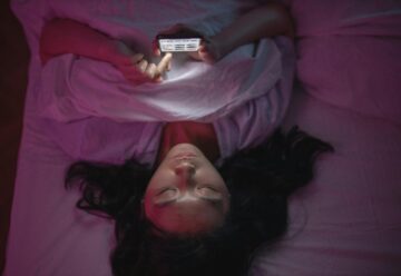 a woman lying on a bed and holding an iPhone for screen time
