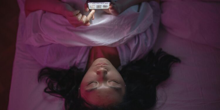 a woman lying on a bed and holding an iPhone for screen time