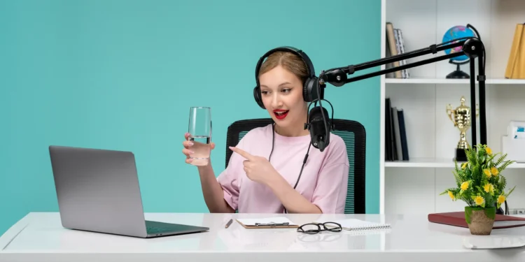woman in front of laptop and mic holding a glass of water and recording one of the best podcasts for motivation